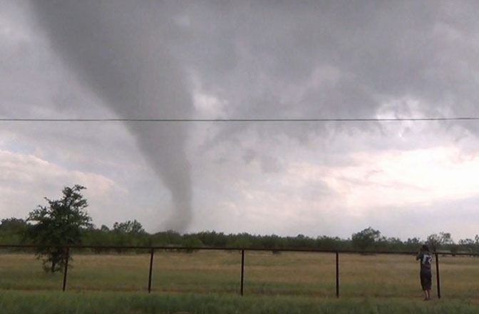 A person take a picture of a distant tornado moving along a flat landscape